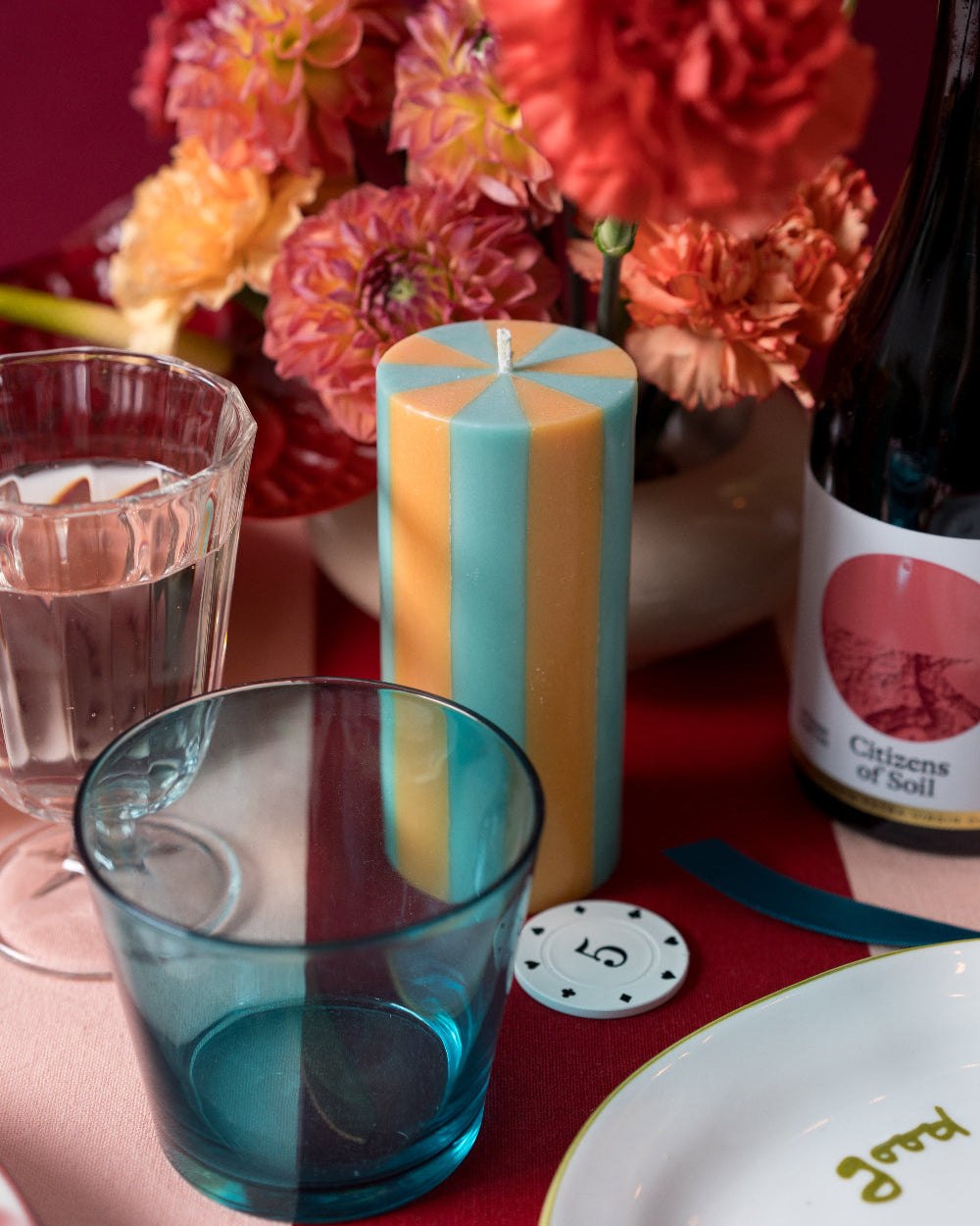 Colorful candle, glasses, and flowers on a table with a bottle of wine.