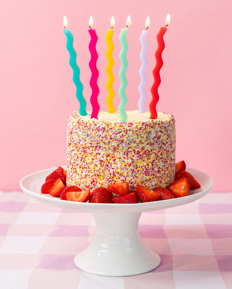 Colorful birthday cake with wavy candles on a pink checkered tablecloth